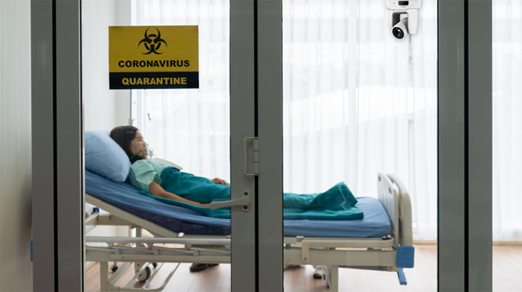 Patient in an isolation ward for highly contagious diseases with a medical grade camera for telesitting and patient monitoring.
